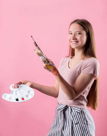 woman artist with a color palette and paintbrushes isolated on pink backgroundの写真素材
