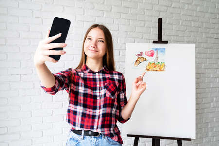 Artist concept. Young teenage girl taking a selfie with her watercolor drawingの写真素材