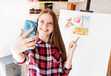Artist concept. Young teenage girl taking a selfie with her watercolor drawingの写真素材