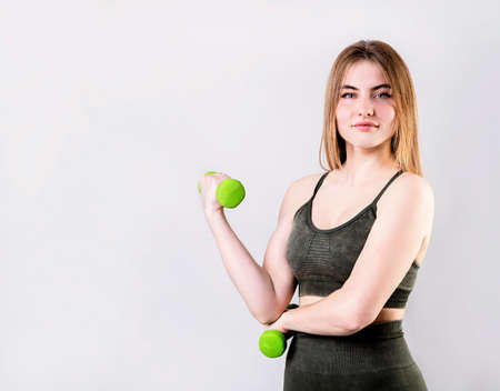 Sport and fitness. Young woman holding green dumbbells isolated on gray backgroundの写真素材