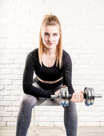 Sportive young smiling woman holding a dumbbell training her bicepsの写真素材