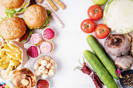 Healthy and unhealthy food concept. Fruits and vegetables vs sweets and fast food top view flat layの写真素材