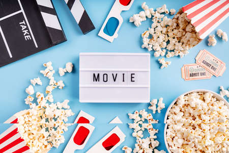 Lightbox with the word Movie, popcorn, 3d glasses and movie tickets top view flat lay on blue solid backgroundの写真素材