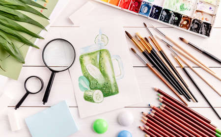 artist workspace with a smoothie sketch, paintbrushes, magnifying glass and watercolor on white wooden background top view flat layの写真素材