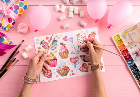 Creative artist workspace. Top view of woman hands drawing the artwork on pink background surrounded with artist suppliesの写真素材