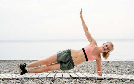 Blonde sportive woman doing exercises at the beach. Athlete woman warming up stretching her arms on...