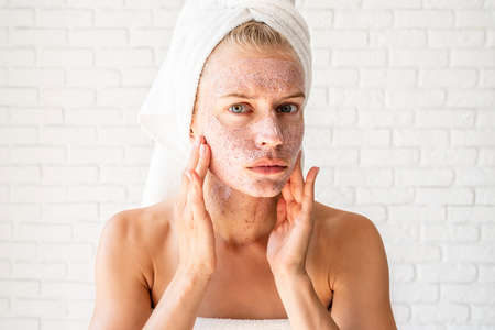Preoccupied young woman in white bath towels applying scrub on her faceの写真素材
