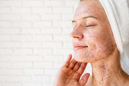 Happy smiling young woman in white bath towels applying scrub on her faceの写真素材