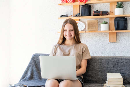 Distance learning. Smiling teenager girl studying using the laptop at home sitting at the sofa