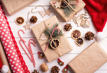 Christmas gifts wrapping. Gift boxes wrappaed in craft paper decorated with pine cones, candy canes and fir tree branches top view flat layの写真素材
