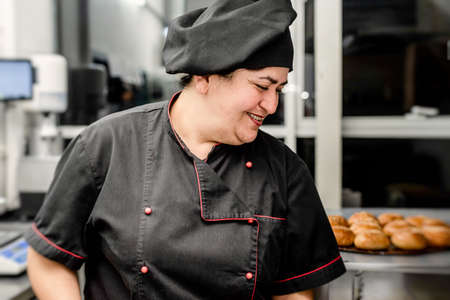 baker in black uniform at the restaurant kitchen holding a pile of fresh bunsの写真素材