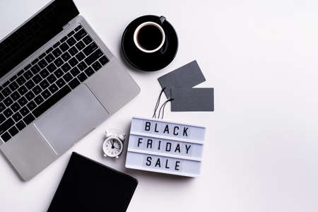 Black Friday Sale words on lightbox with cup of coffee, laptop and clock top view flat lay on white...