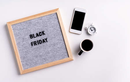 Black friday, seasonal sale concept. Text black friday on gray letter board with mobile phone, coffee and alarm clock on white backgroundの写真素材
