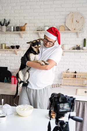Christmas cooking. Chef in santa hat holding his dog in the arms cooking in the kitchen and making...