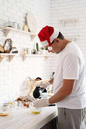 Christmas baking concept. Man in santa hat making meringue on white wooden table. Meringue recipe