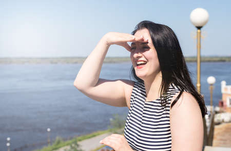 Happiness concept. Young laughing woman standing by the riverside enjoying the view covering her...