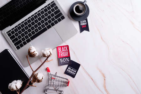 Black Friday Sale words on the tag, workspace with laptop, notebook and shopping cart top view flat lay with copy spaceの写真素材