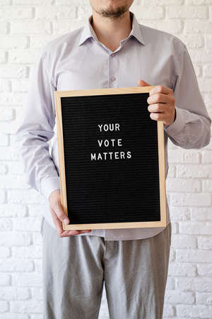 Black letter board with the text your vote matters with American flag on white marble background