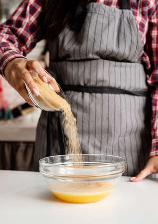 Young latin woman pouring sugar to the dough cooking at the kitchenの写真素材