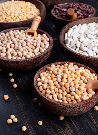 Various dried legumes in wooden bowls on wooden rustic background
