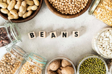 Various dried legumes in wooden bowls with the text Beans top view flat lay on white marble backgroundの写真素材