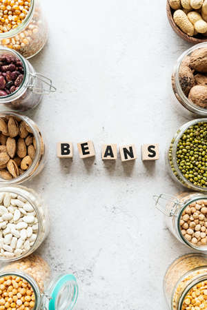 Various dried legumes in wooden bowls with the text Beans top view flat lay on white marble backgroundの写真素材