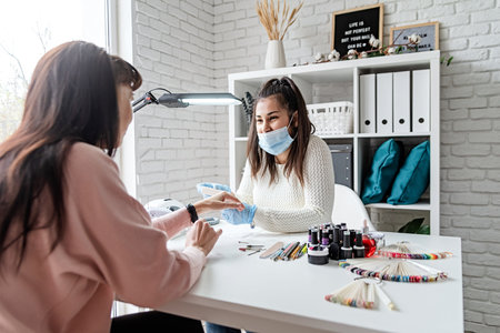Manicure and pedicure salon. Manicure master in mask and gloves putting on gel polish on the nails of a clientの写真素材