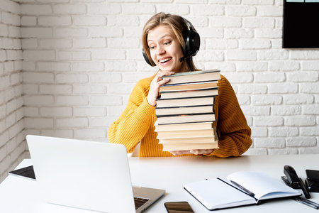 Distance learning. E-learning. Young smiling woman in black headphones studying online using laptop...