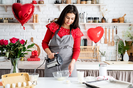 Valentines Day. Woman in red dress and gray apron making valentine cooking at the kitchenの写真素材