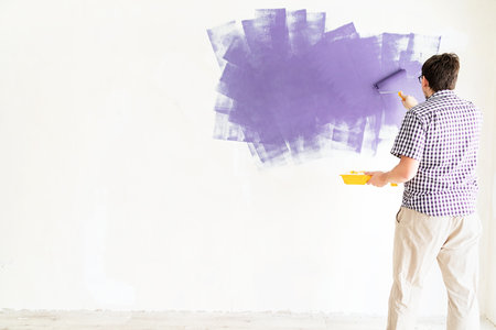 Home repair and improvement. Man coloring wall purple with a rollerの写真素材