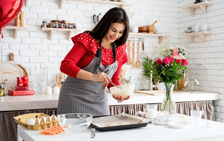 Woman in red dress and gray apron making valentine cookies at the kitchenの写真素材