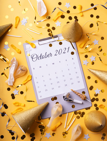 October 2021 calendar with confetti, birthday hats and balloons top view flat lay on yellow backgroundの写真素材
