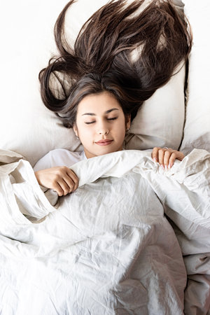 Valentine's Day. Sleeping. Young happy brunette woman sitting awake in the bed with red heart shaped...