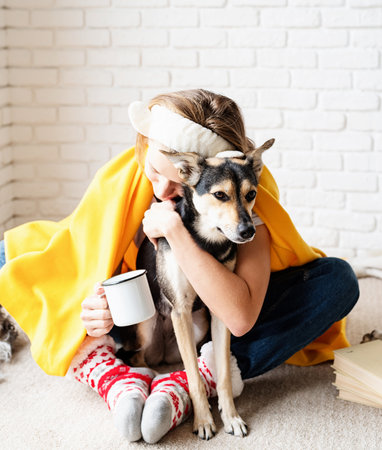 Pet care. Funny young woman in yellow plaid sitting on the floor with her dogs drinking coffeeの写真素材