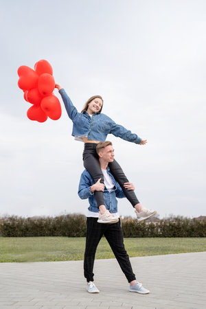 Happy young loving couple embracing each other outdoors in the park having fun holding red balloons
