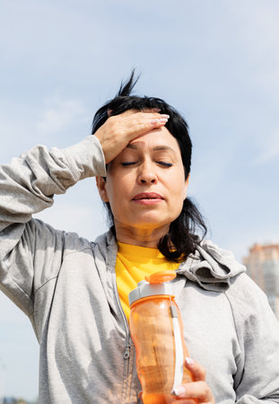 senior woman wiping out sweat after hard workout outdoors in the parkの写真素材