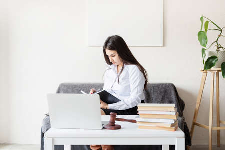 Pretty young woman enjoying reading a book at home sitting on the sofa smiling in pleasure in casual...