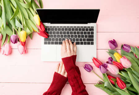Easter and spring concept. Top view of laptop computer, colorful tulips and Easter eggs on pink wooden backgroundの写真素材