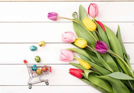 Shopping cart with colorful bouquet of tulips on white wooden backgroundの写真素材