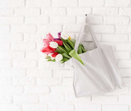 Eco friendly, zero waste concept. Gray fabric bag full of colorful tulips on white brick backgroundの写真素材