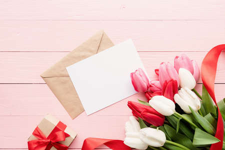 Frame mock up with Greeting card and envelope with colorful spring tulips top view over pink wooden...