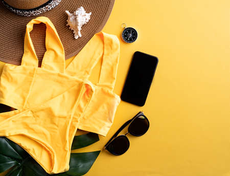 Travel and adventure. Flat lay traveling gear with swimsuit, smartphone, sunglasses and compass on yellow background with copy spaceの写真素材