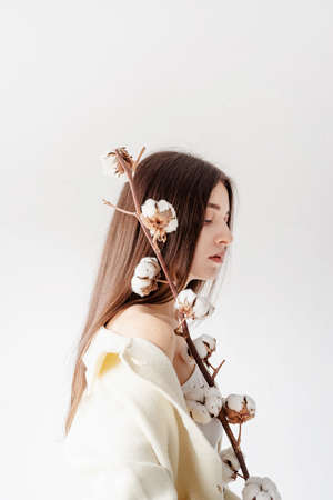 Beauty and youth Concept. Beautiful woman in cozy clothes holding branch of cotton flowersの写真素材