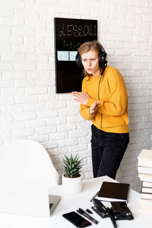 Distance learning. E-learning. Young smiling woman in yellow sweater and black headphones studying online using laptop, sitting on the couch at homeの写真素材