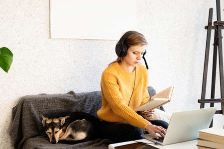 Distance learning. E-learning. Young smiling woman in yellow sweater and black headphones studying...