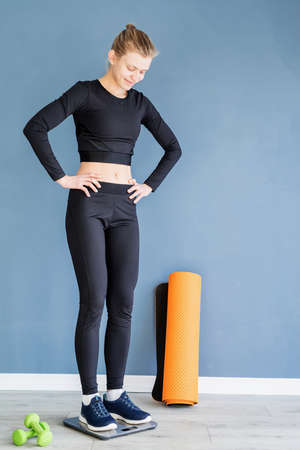 Dieting and weight loss. Woman in black sport clothes standing on scalesの写真素材