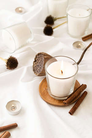 Home decoration and interior. Beautiful burning candles with cinnamon and dry flowers on white fabric backgroundの写真素材