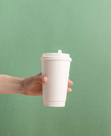 Eco friendly zero waste disposable tableware. Woman hand holding white large takeaway paper coffee cup mock up on green backgroundの写真素材