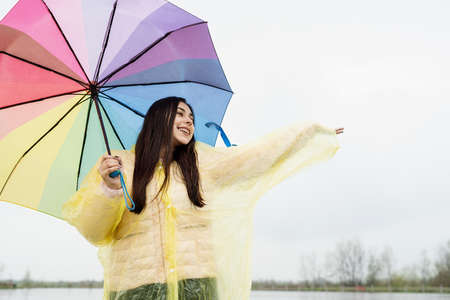 Beautiful brunette woman holding colorful umbrella out in the rainの写真素材