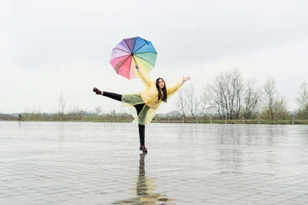 Beautiful brunette woman holding colorful umbrella dancing in the rainの写真素材
